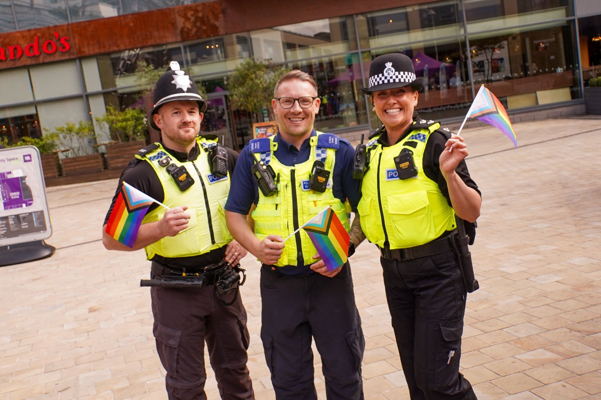 Three police officers are standing next to each other holding rainbow flags.