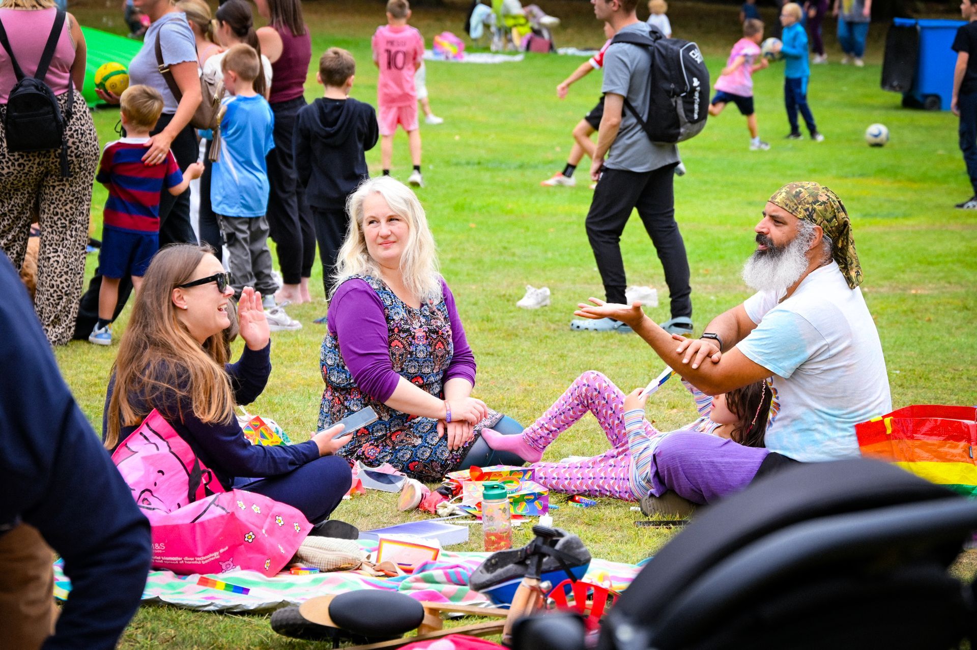 People on a stage hold up LGBTQ+ pride flags, smiling. They wear bright pink and orange clothing.