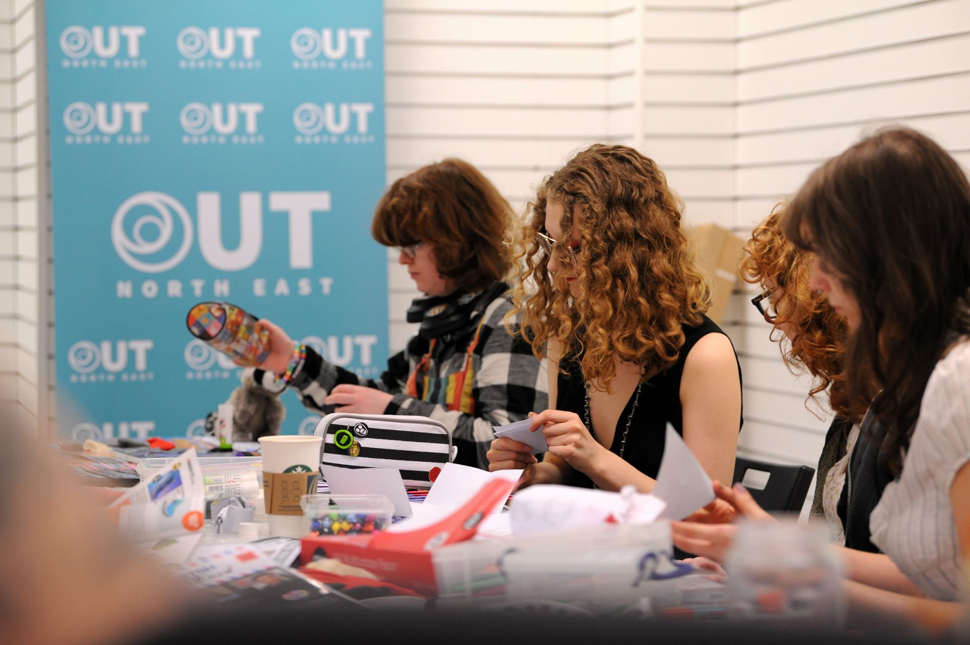 Four women sit at a table in front of a sign that says out north east