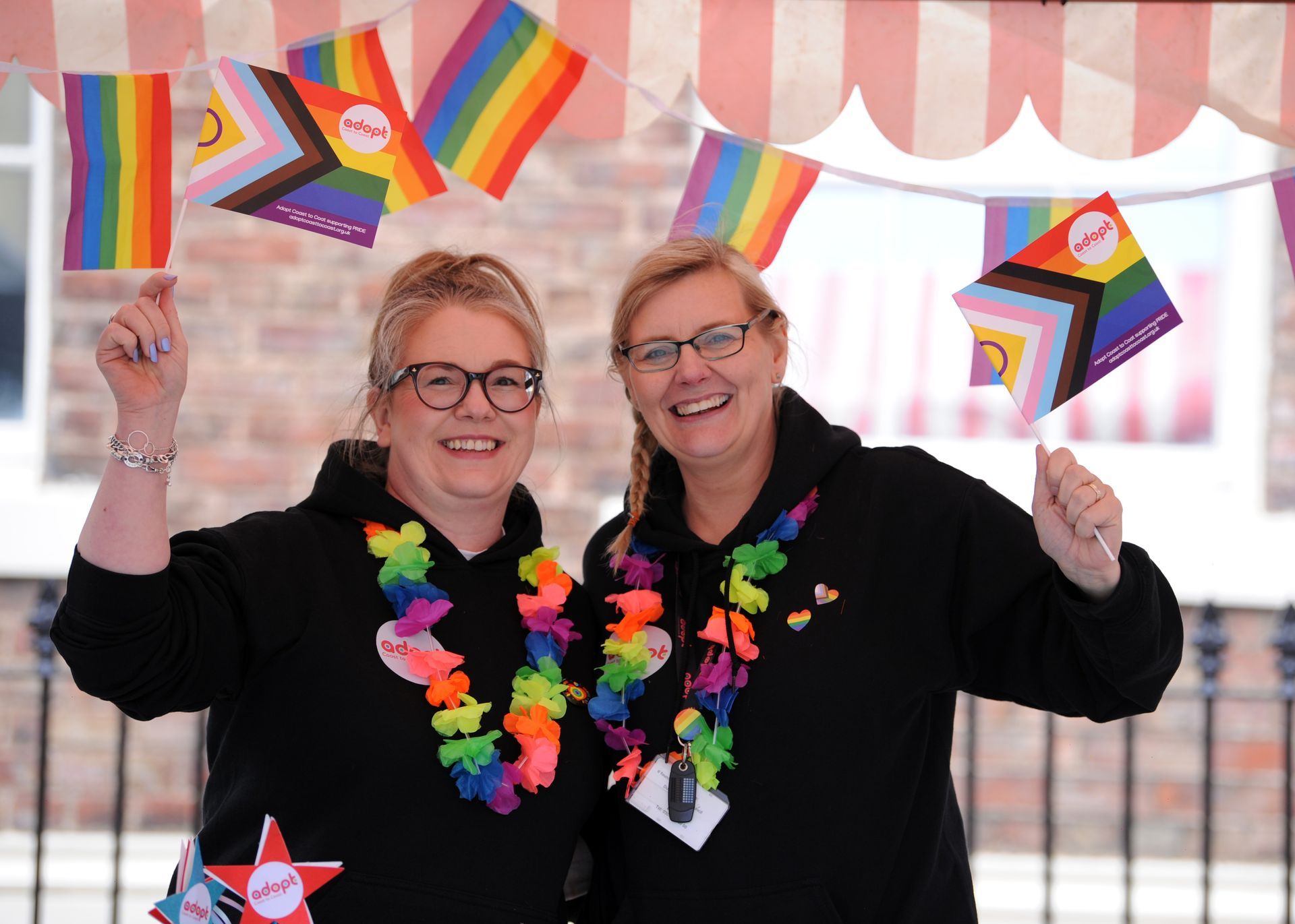 Two women are standing next to each other holding rainbow flags.
