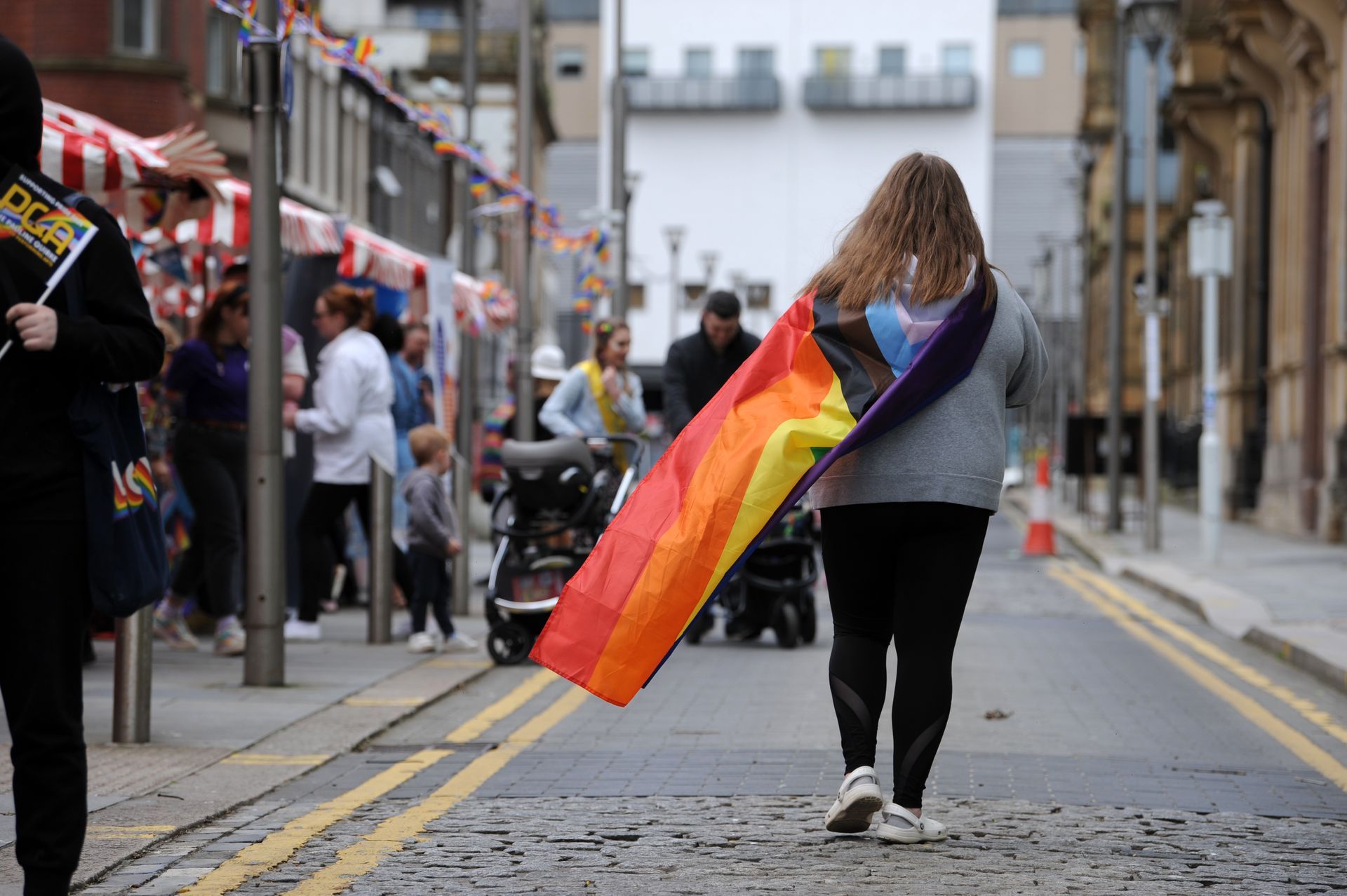 A woman is walking down a street holding a rainbow flag.