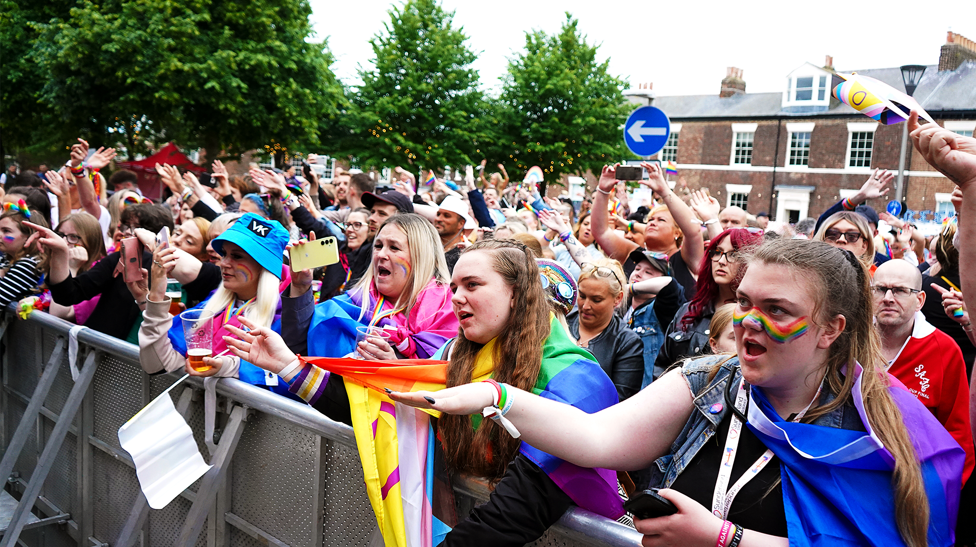 A crowd of people standing behind a metal fence at a concert.