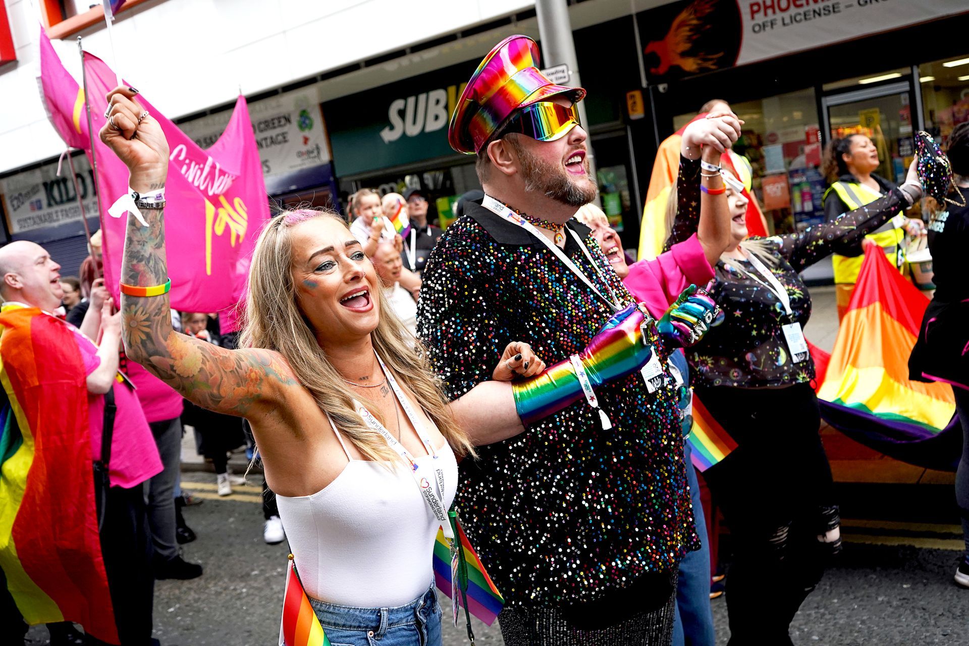A group of people are standing in front of a store holding rainbow flags.
