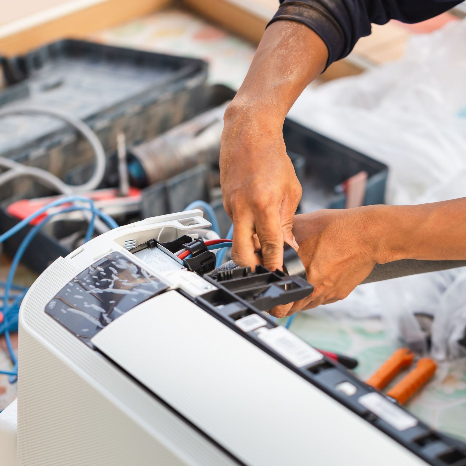 Person working on a white air conditioner; hands visible, tools nearby.