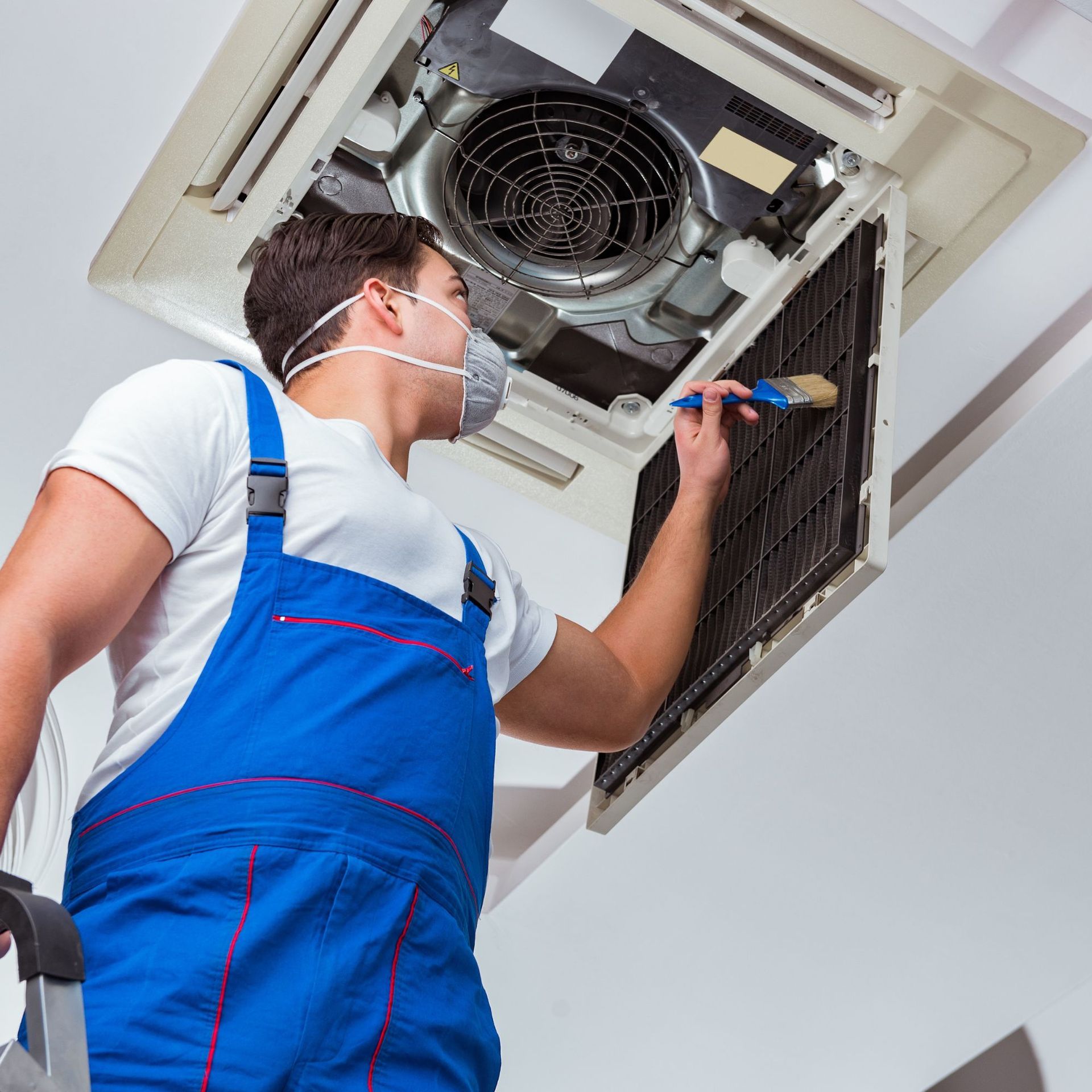 Above Comfort Mechanical LLC - HVAC technician in blue overalls cleans an air conditioning unit. 