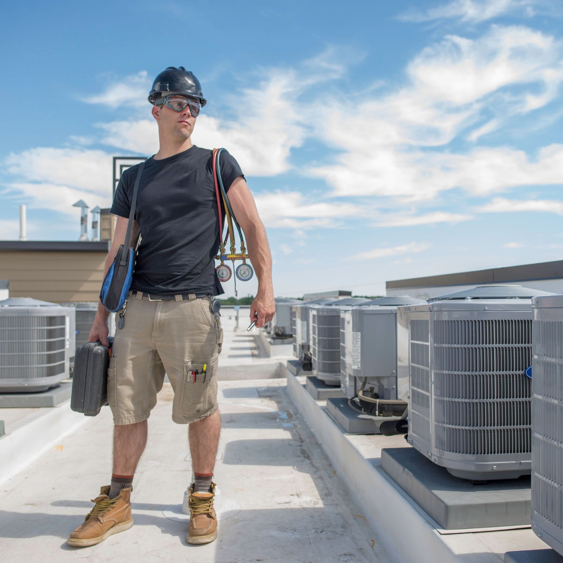 Above Comfort Mechanical LLC - HVAC technician on a rooftop, wearing a hard hat and carrying tools.