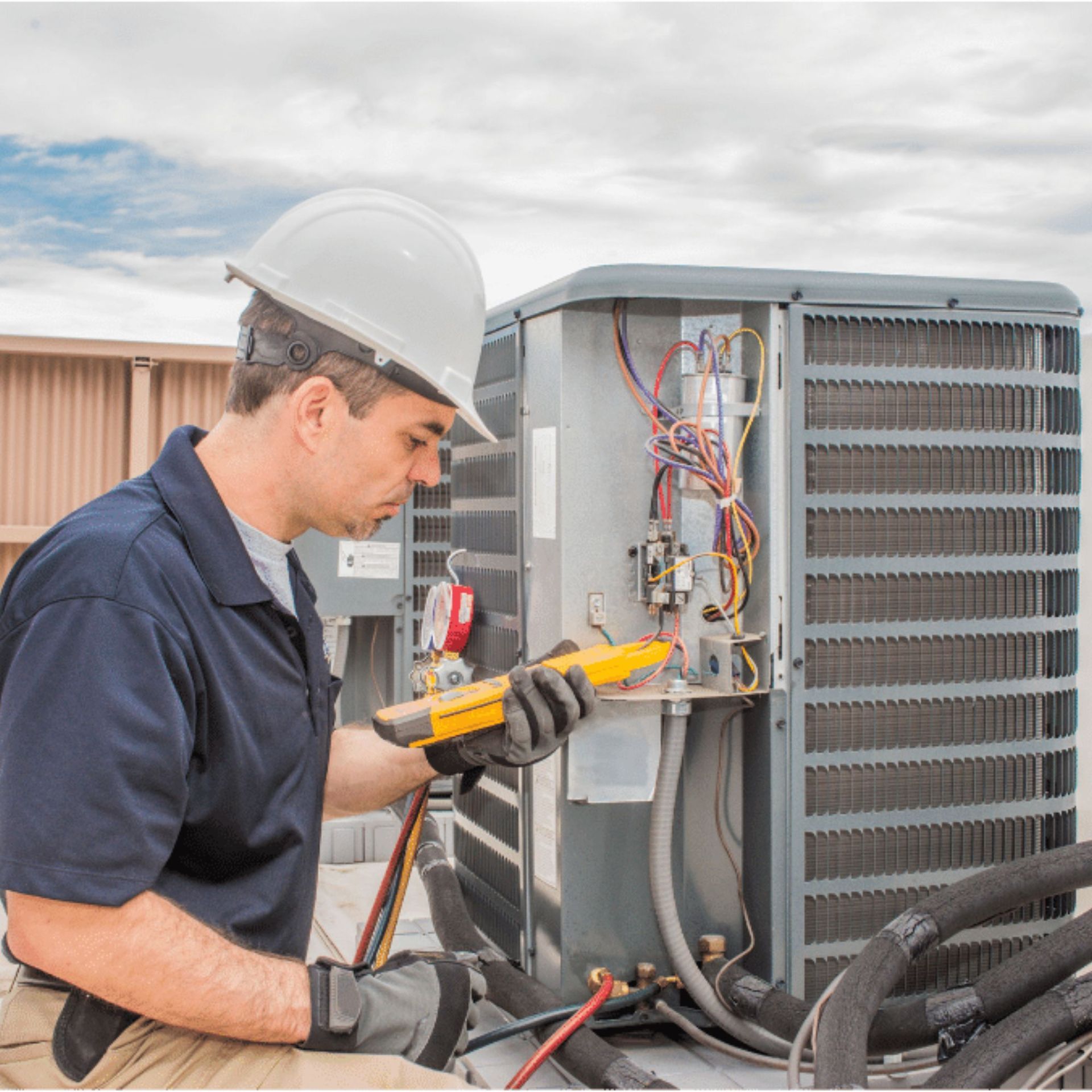 HVAC technician in a hard hat examines an air conditioning unit on a rooftop with a yellow multimeter.