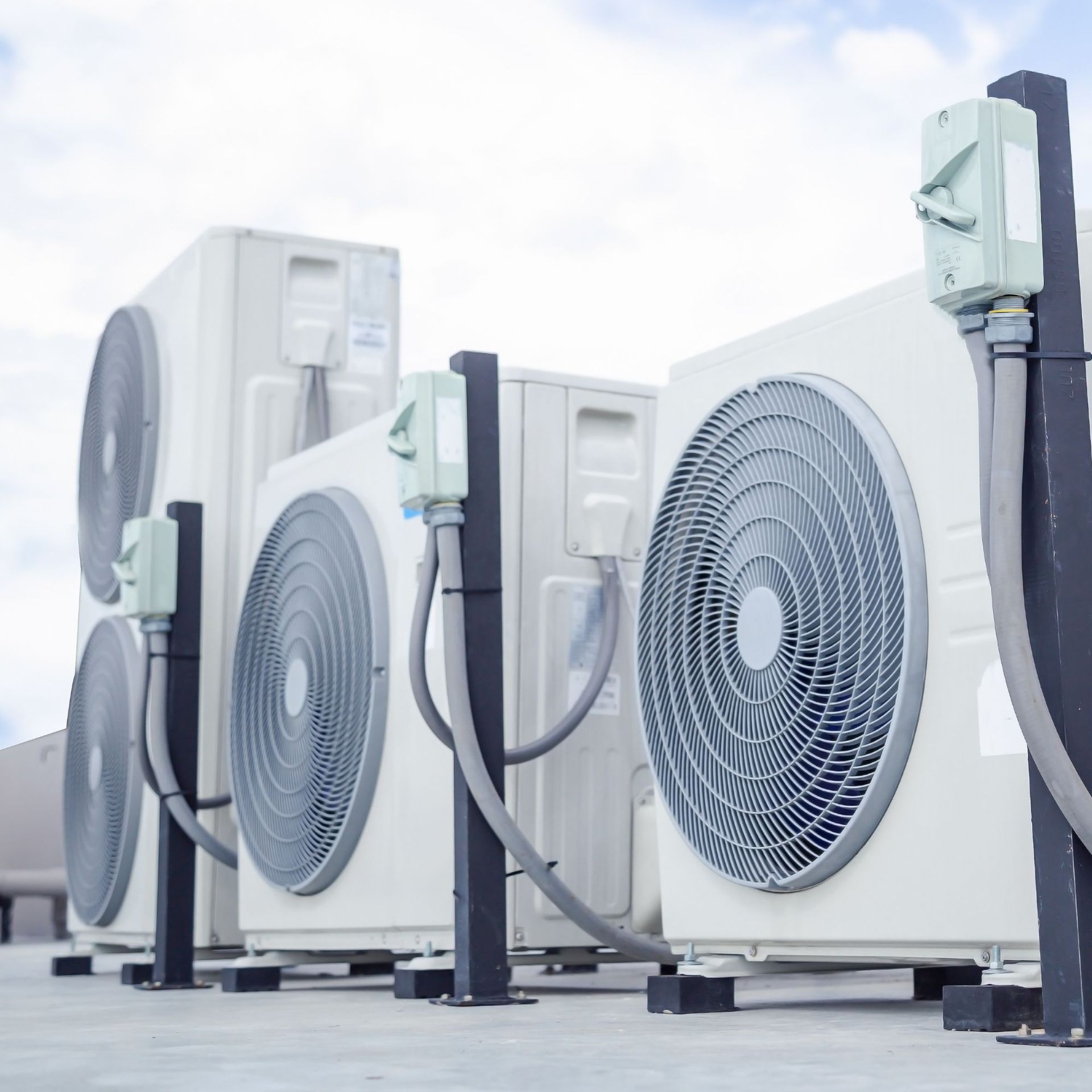 Air conditioning units on a rooftop; white, with gray fan blades, connected by gray tubes, against a blue sky.