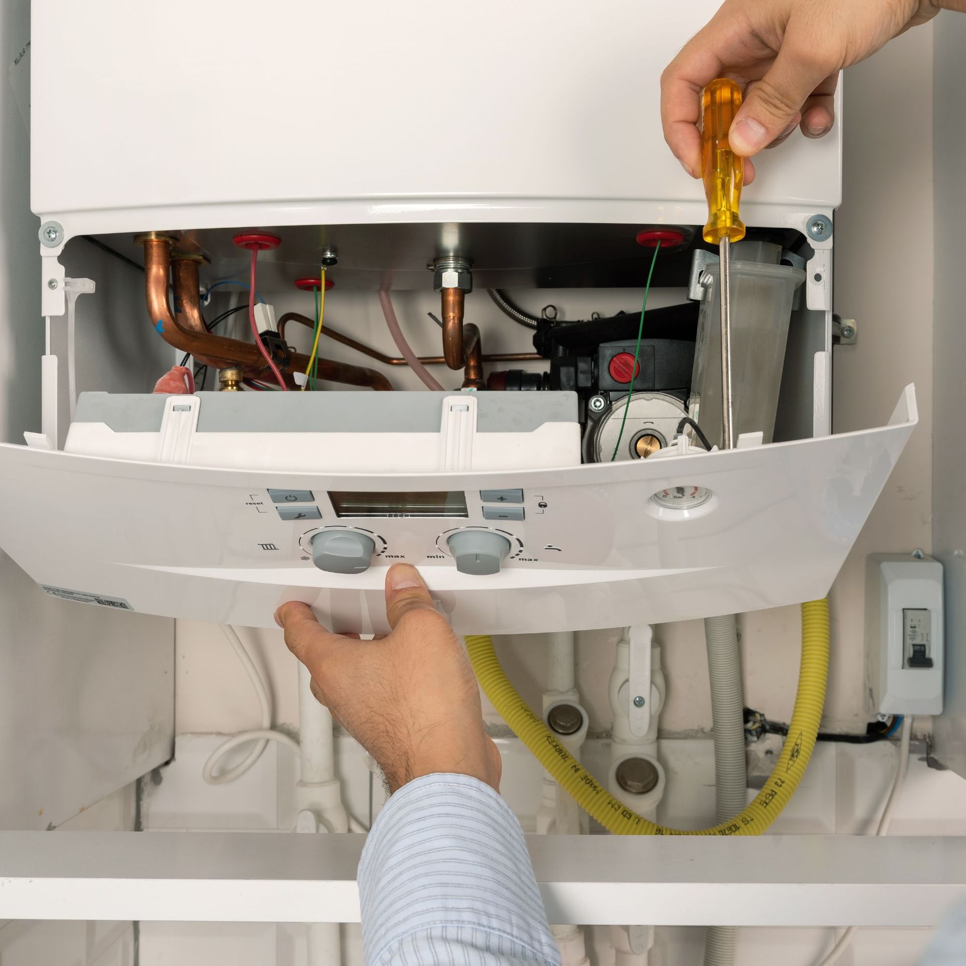 Above Comfort Mechanical LLC - A person repairing a white boiler with a screwdriver; hands visible, indoor setting.