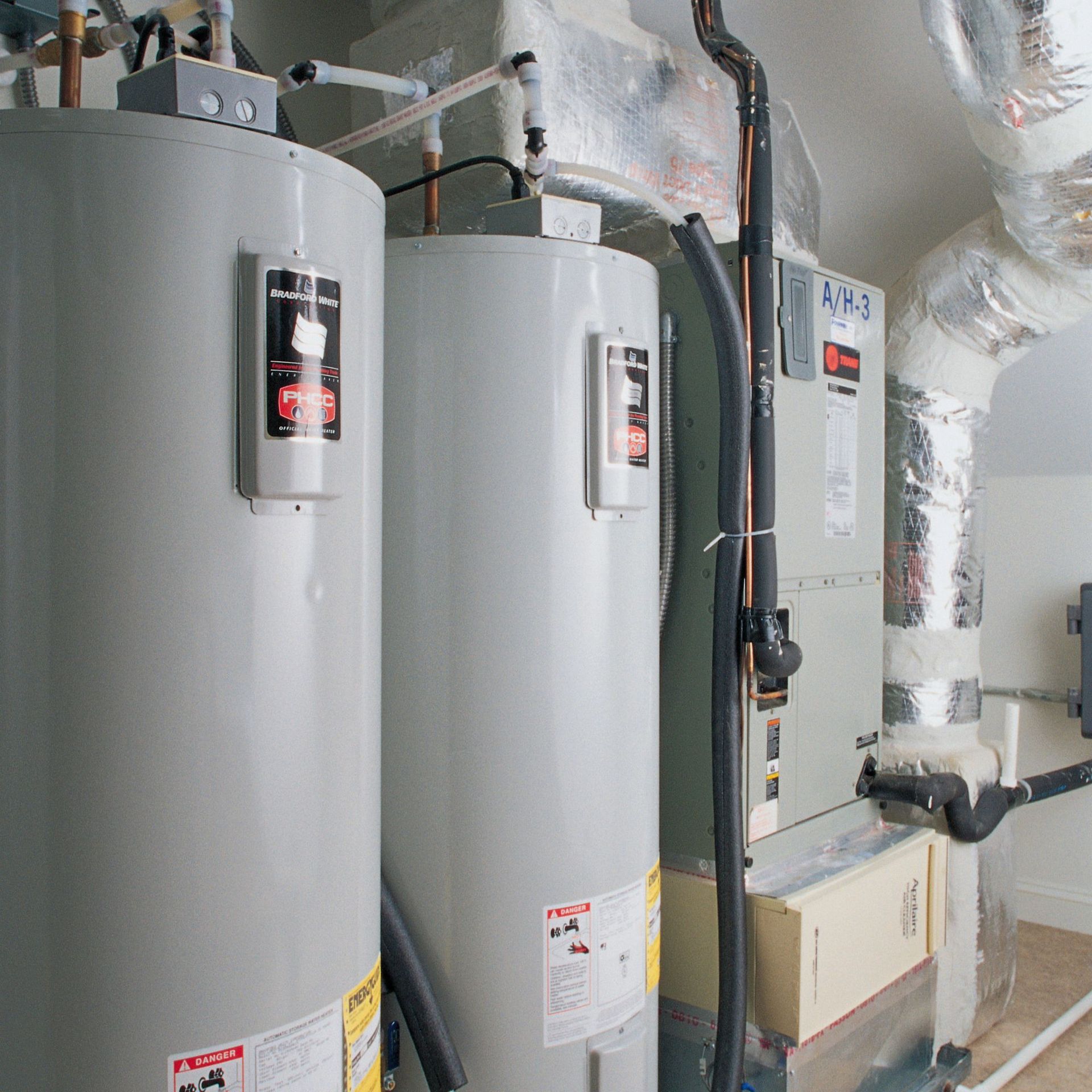 Above Comfort Mechanical LLC - Two large gray water heaters and a furnace in a utility room.