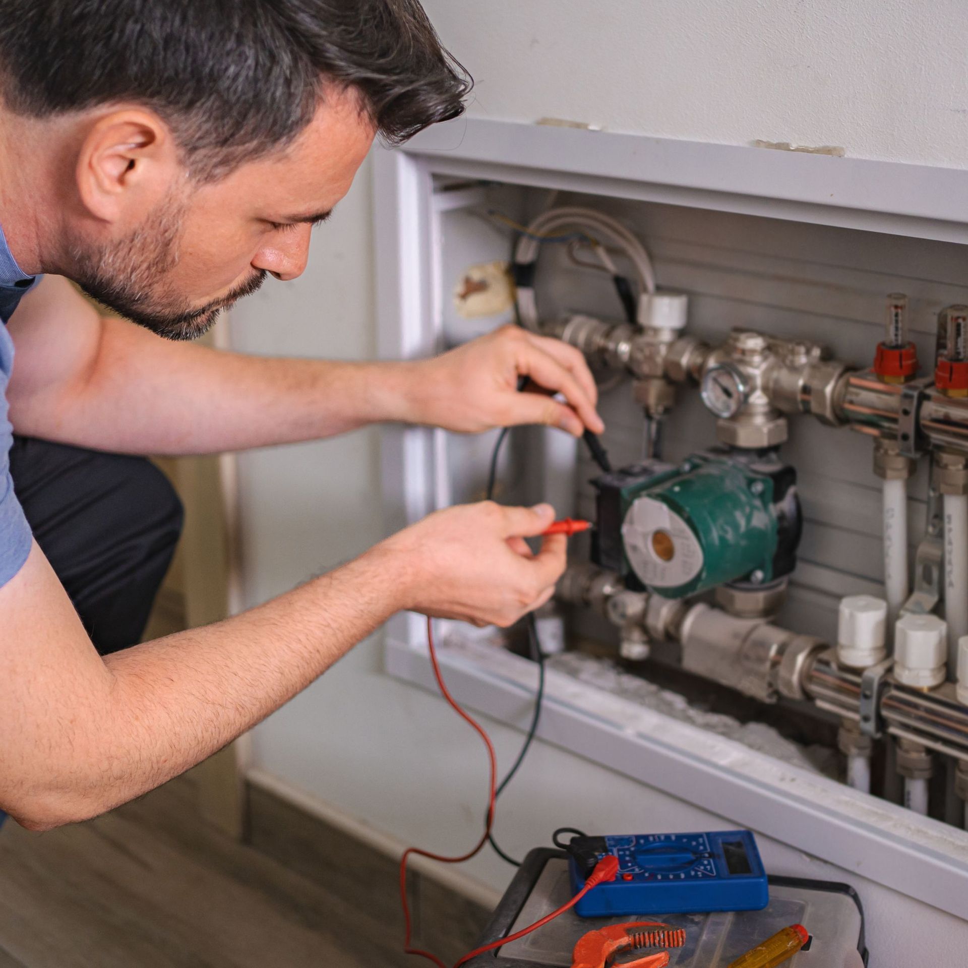 Man in blue shirt tests wires connected to heating system, using a multimeter.