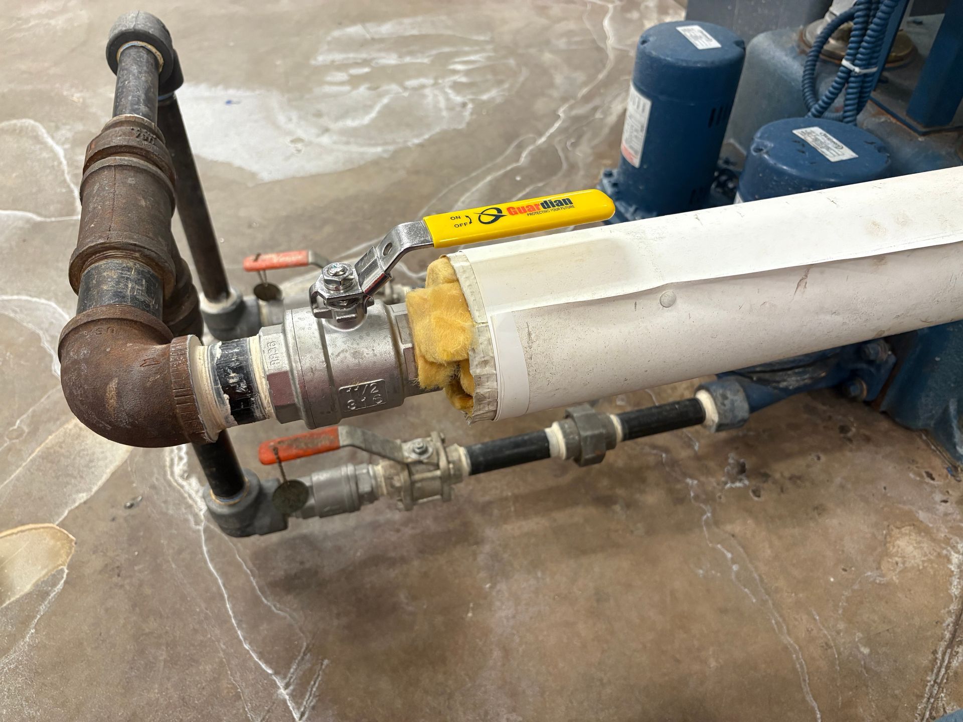 Pipes and valves connected to a blue pump, with white insulation and a silver handle on a yellow valve.