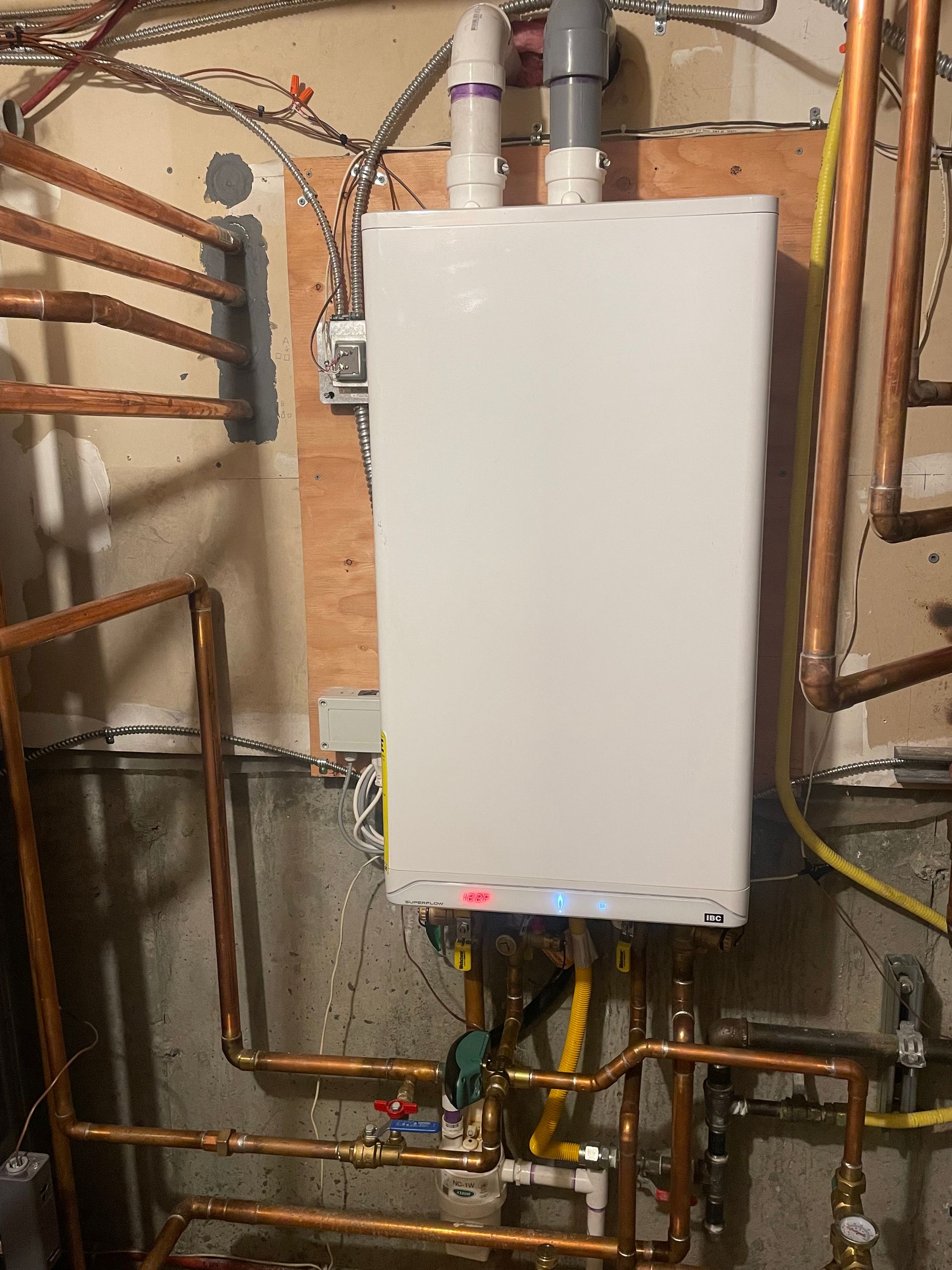 White wall-mounted boiler with copper piping, in a basement setting.