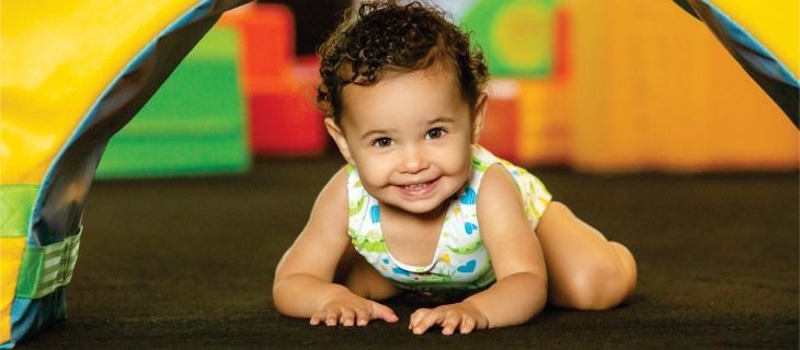 A baby is crawling on the floor under a tent and smiling.