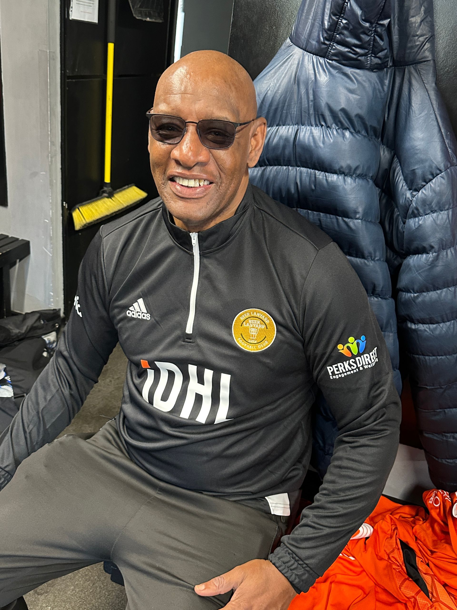 A bald man wearing sunglasses and a black shirt with the word dhj on it