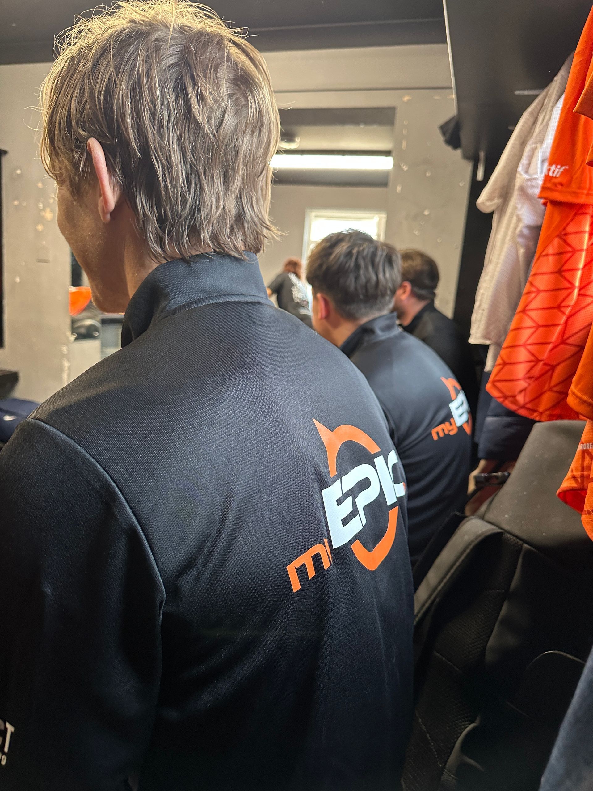 A man wearing a black epic shirt stands in a locker room