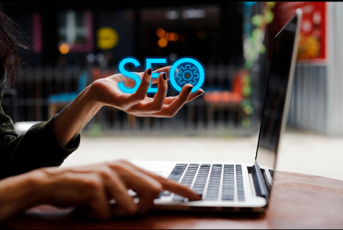 A person is typing on a laptop and holding up the word seo