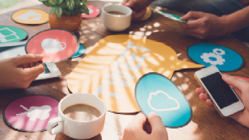 A group of people are sitting around a table with cups of coffee and a cell phone.