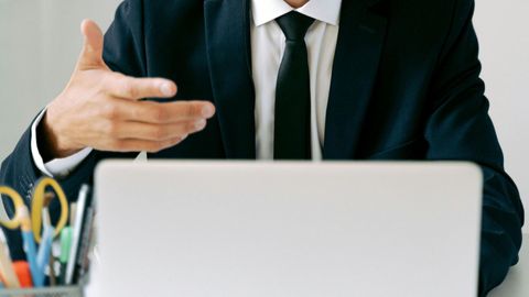 A man in a suit and tie is sitting at a desk in front of a laptop computer.