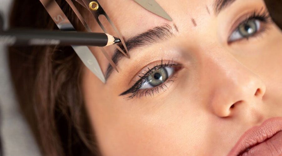 Einer Frau werden mit Bleistift und Schere die Augenbrauen nachgezogen.