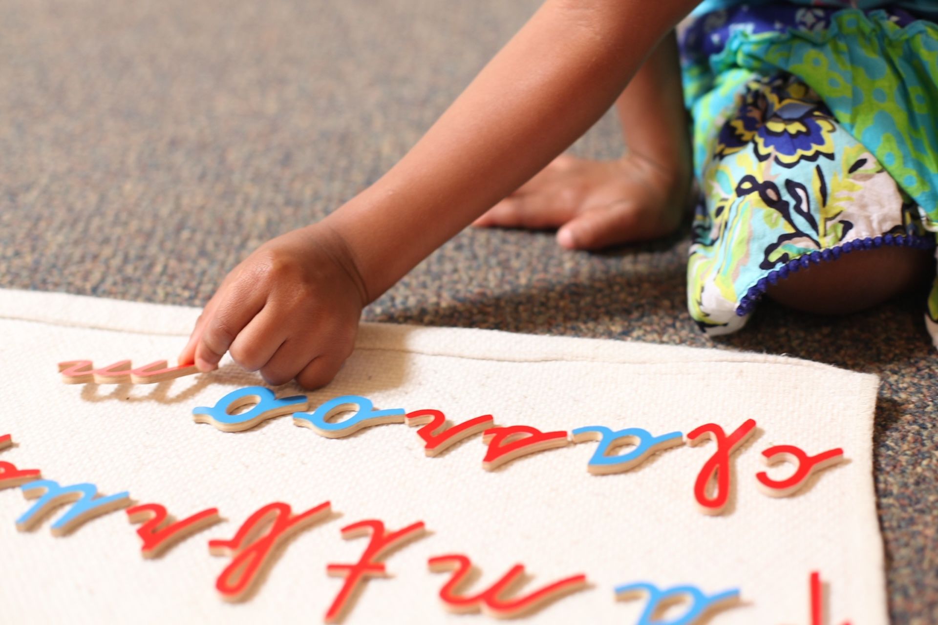 Hand placing colorful letters on a white rug during a learning activity