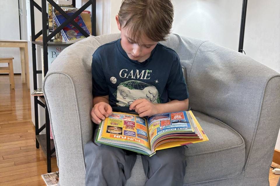 Montessori child reading a book in cozy space, building focus, imagination, and love of stories.