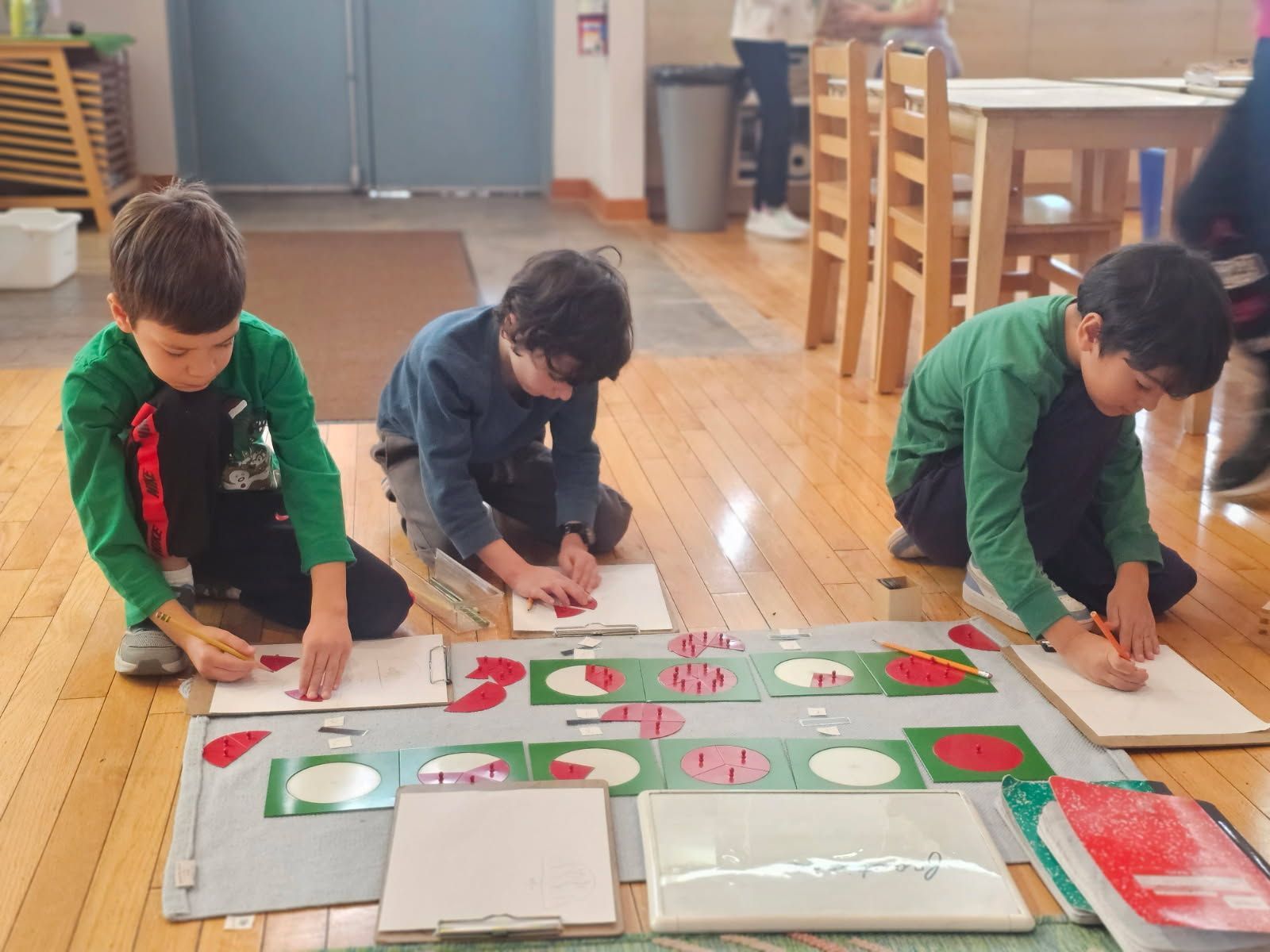 Three children on a wooden floor, coloring and working on art project.