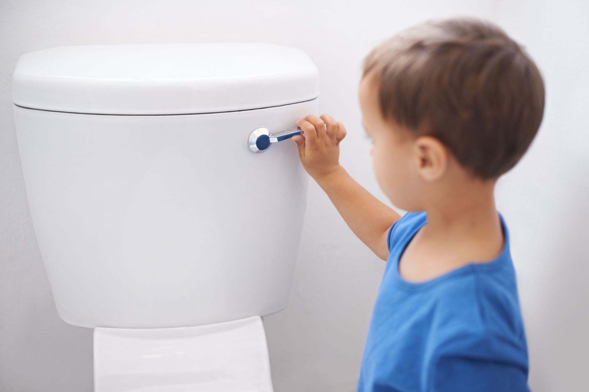 Child in blue shirt reaching for toilet handle.