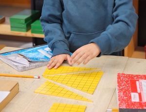 Child using a ruler to measure and cut yellow grid paper.