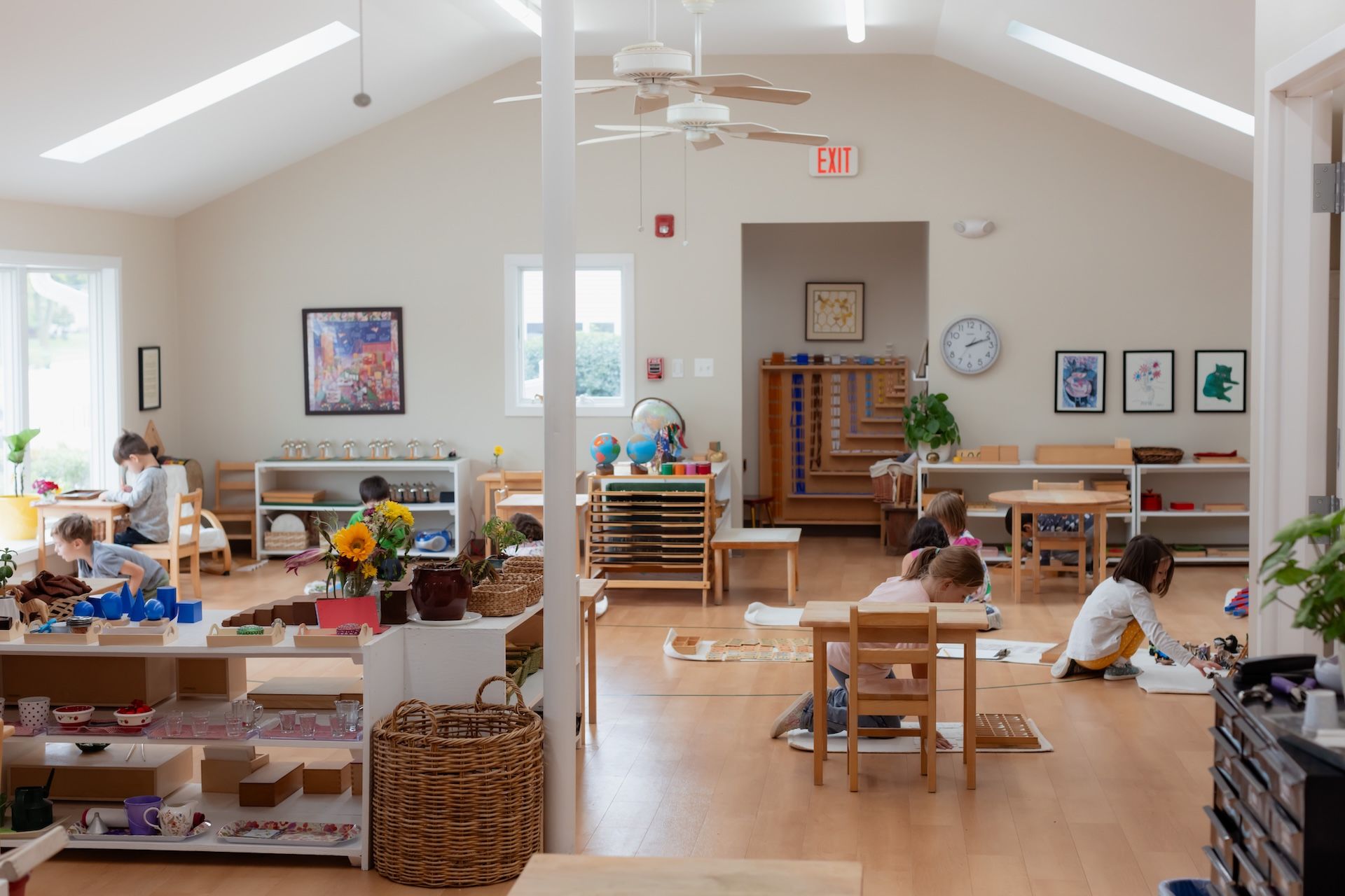 Bright classroom with children working at tables, wooden toys, and colorful wall art