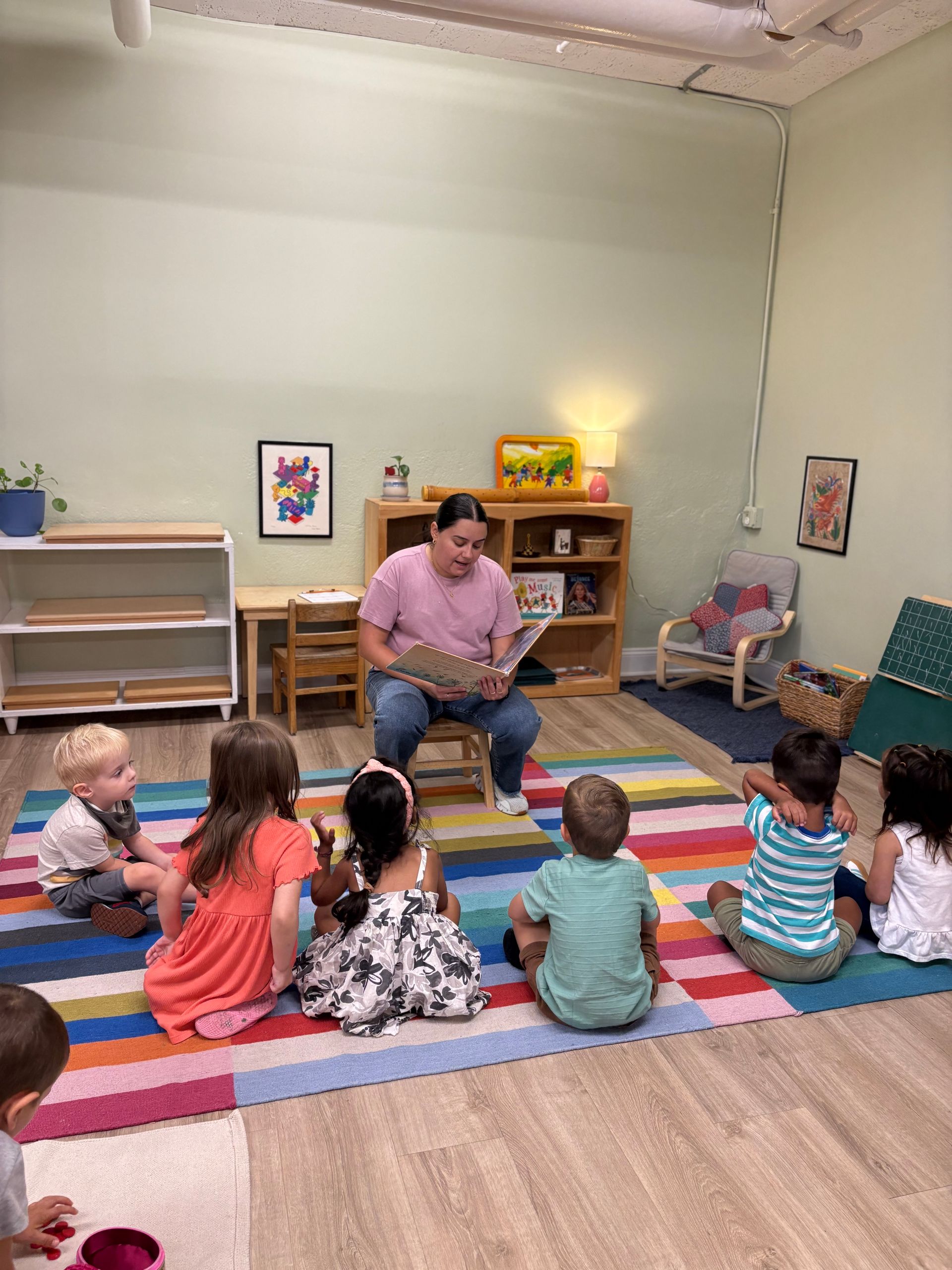 Teacher reading with young children, modeling attentive adult presence in early learning.
