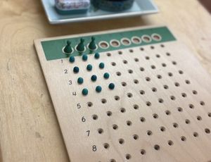 Wooden multiplication board with pegs and beads on a wooden table.