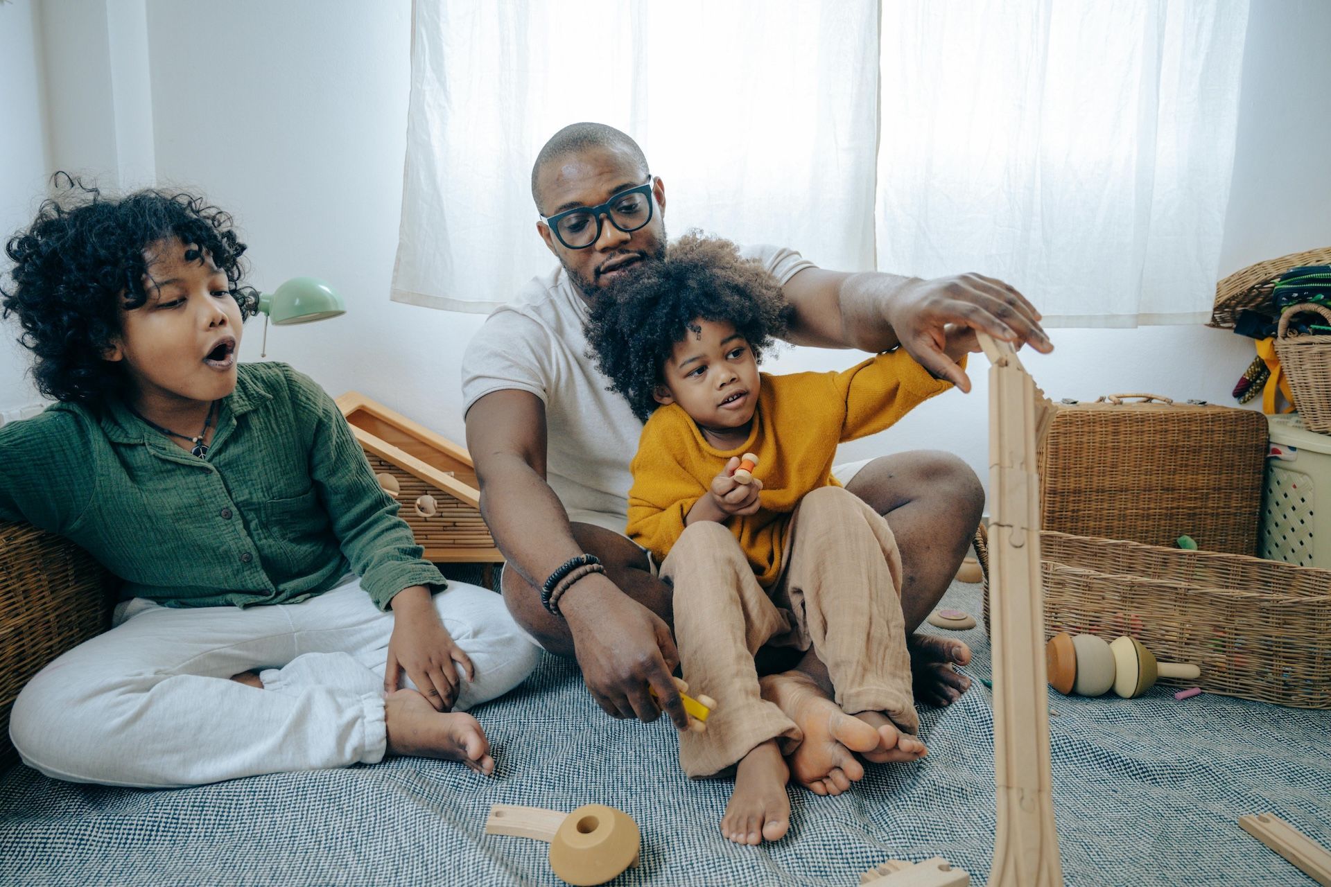 Three people sitting on a rug, playing with a wooden toy in a bright room.