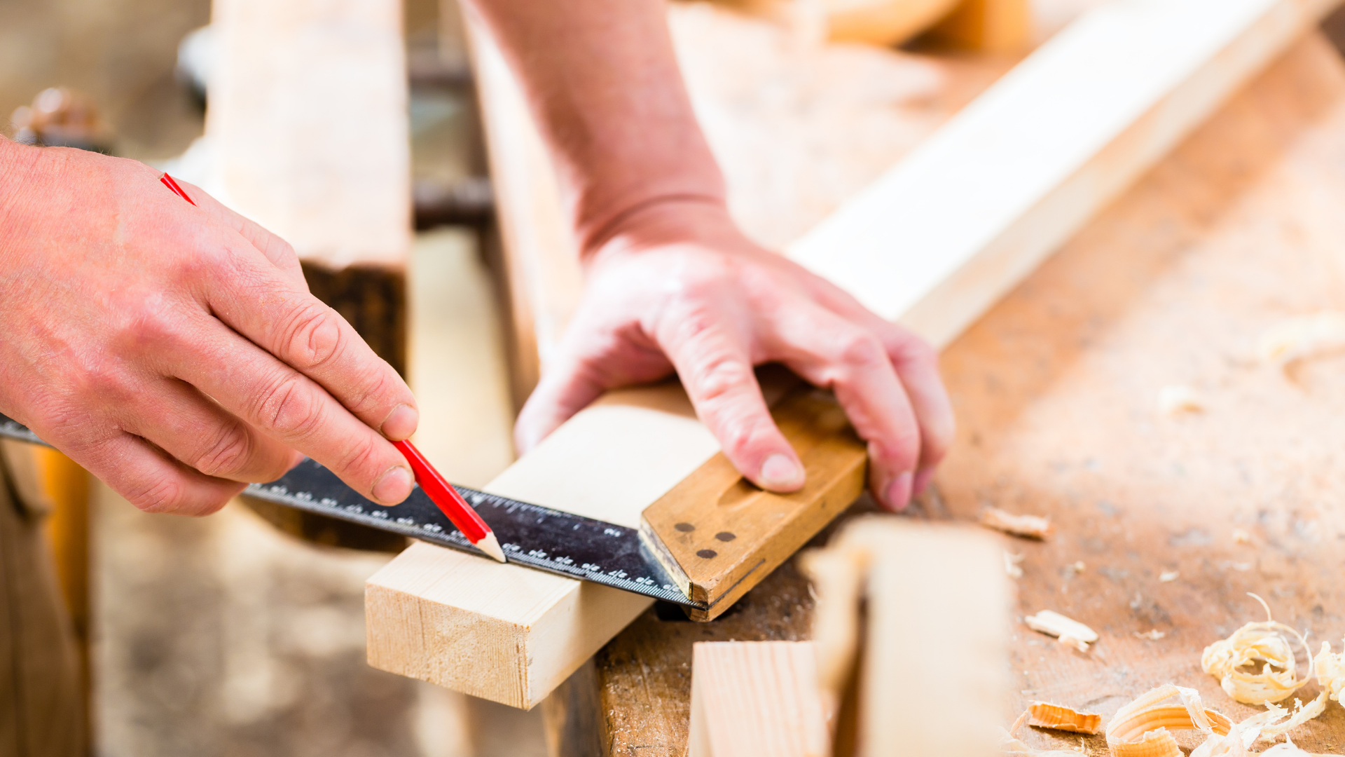 Person using a square to measure and mark wood with a pencil in a workshop.