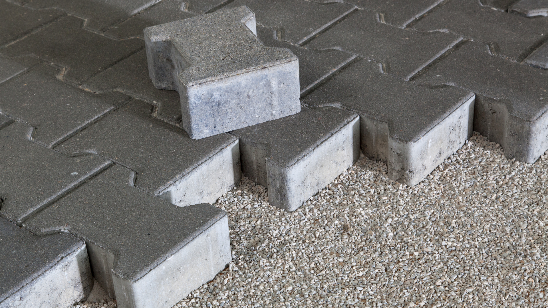 Gray concrete interlocking paving stones being laid on gravel.