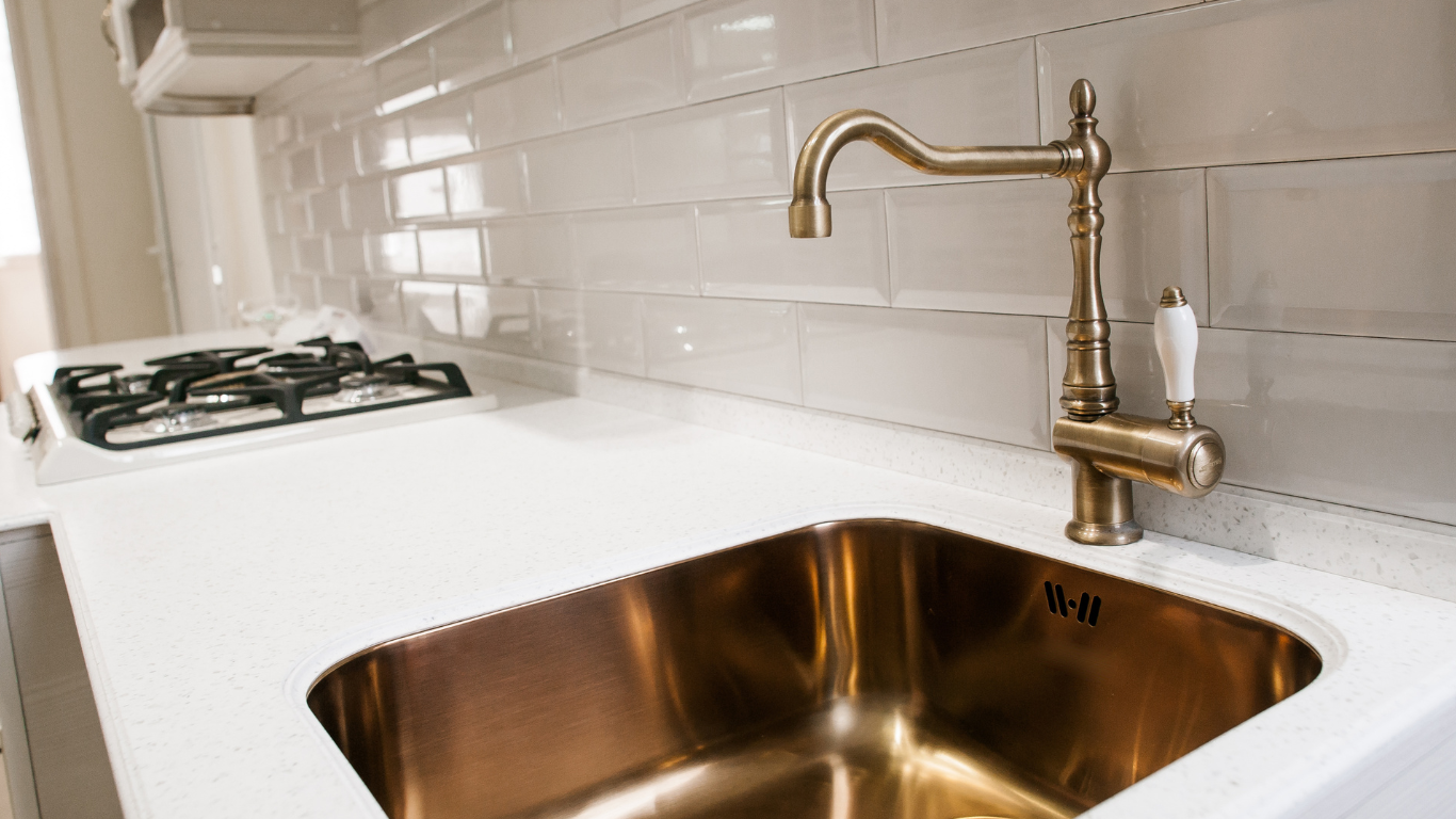 Plumber kneeling under a sink, repairing pipes. Tools are scattered nearby; washing machine in background.