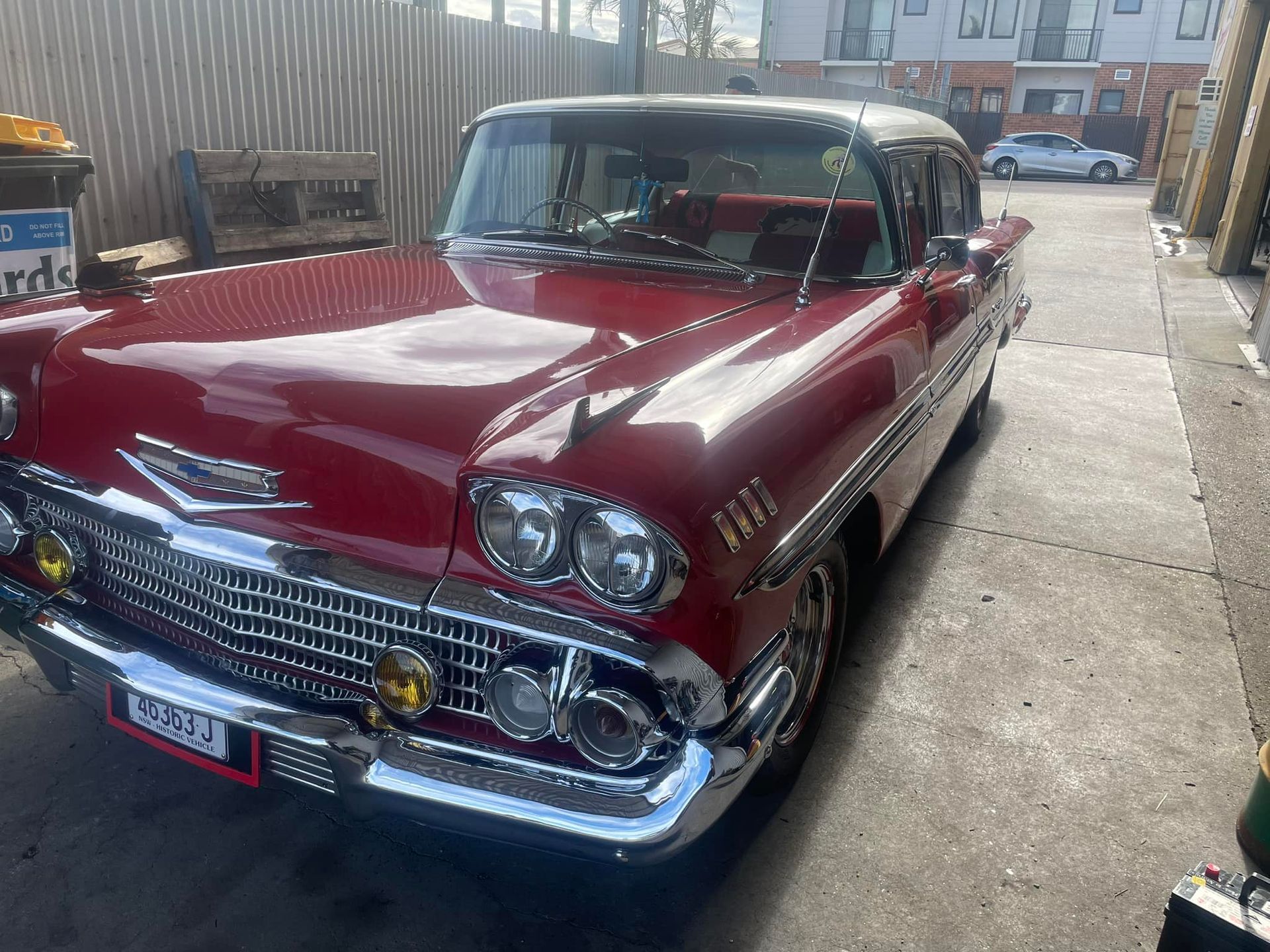 A red, vintage Chevrolet with chrome trim parked outdoors on a concrete lot. 