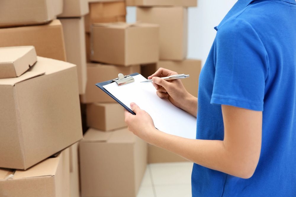 A Woman Is Writing On A Clipboard In Front Of A Pile Of Cardboard Boxes — CC Couriers FNQ in Portsmith, QLD