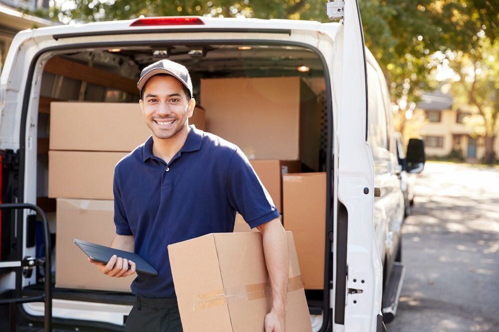 A Delivery Man Is Standing In Front Of A Van Holding A Cardboard Box And A Tablet — CC Couriers FNQ in Portsmith, QLD