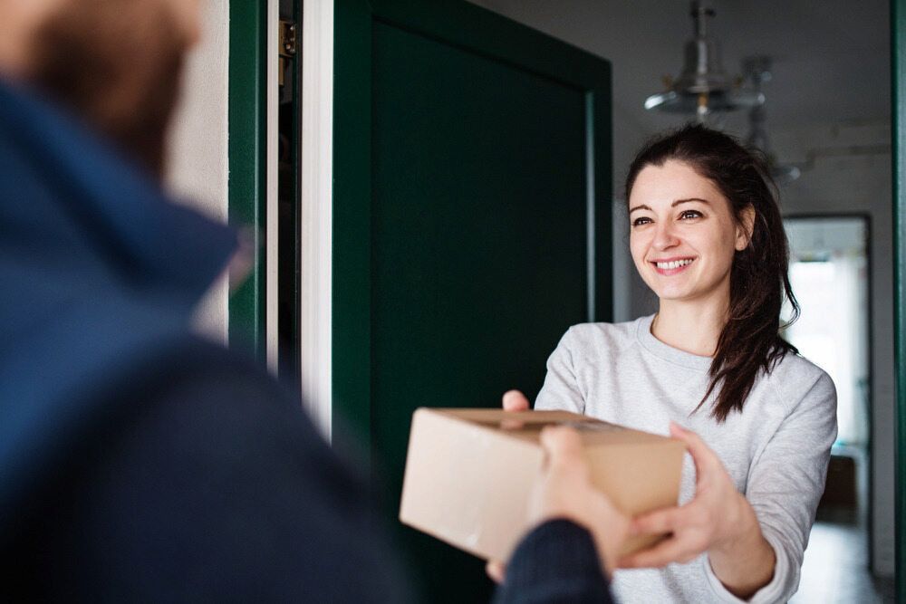 A Woman Is Handing A Package To A Man In A Doorway — CC Couriers FNQ in Tablelands, QLD