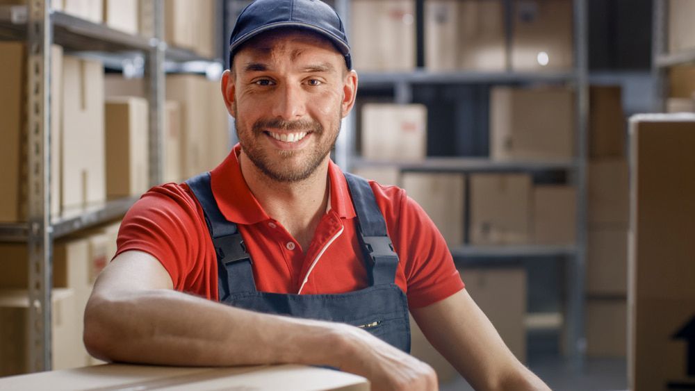 A Delivery Man Is Leaning On A Box In A Warehouse And Smiling — CC Couriers FNQ in Portsmith, QLD