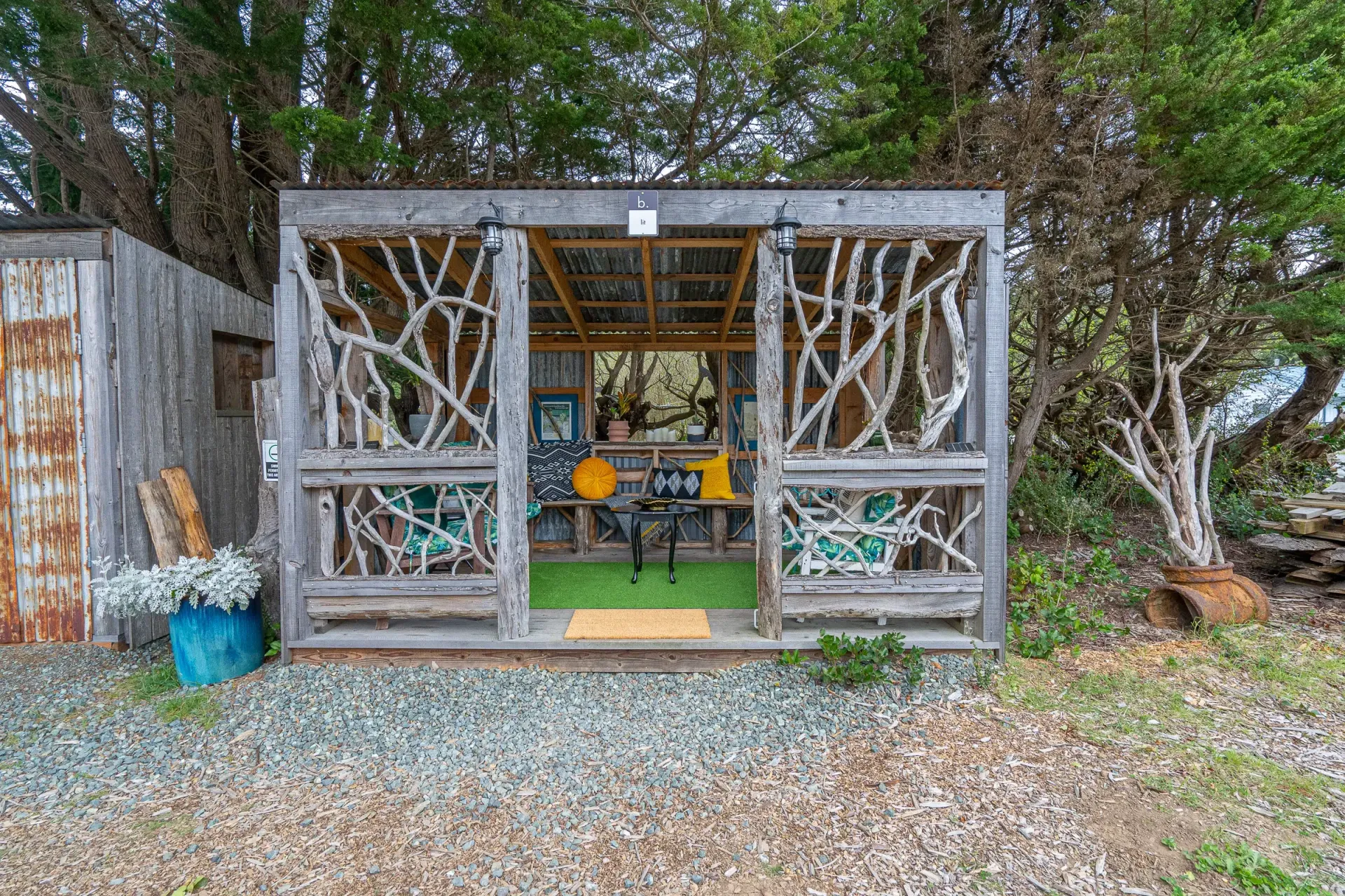 A wooden gazebo with a table and chairs in the middle of a forest.