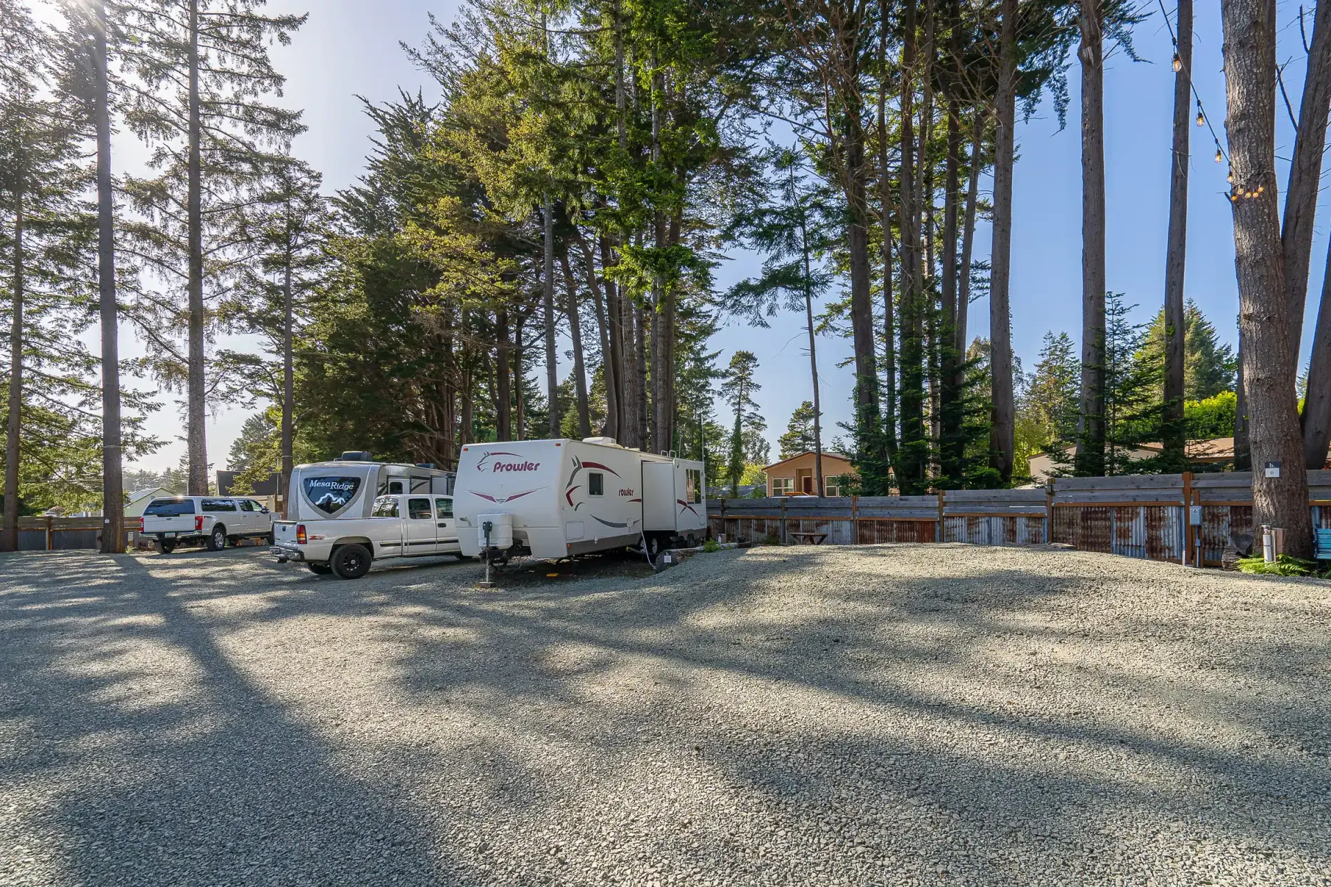 A group of rvs are parked in a gravel lot surrounded by trees.