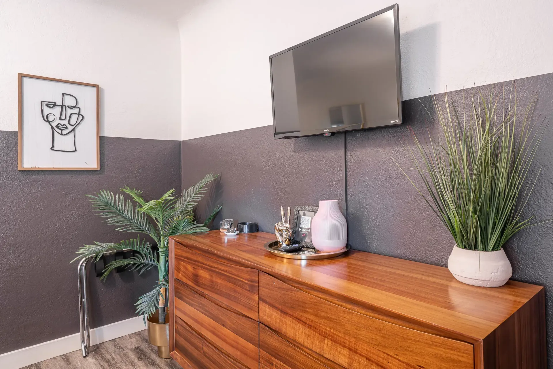 A living room with a wooden dresser and a flat screen tv on the wall.