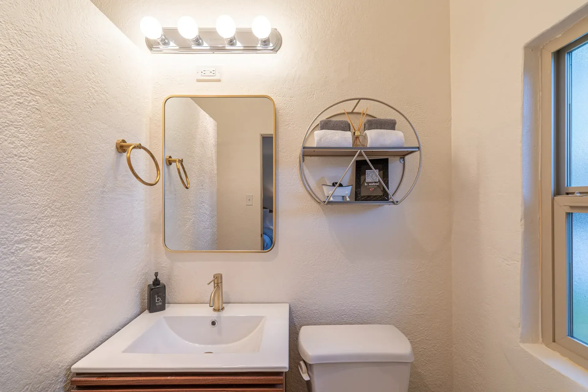 A bathroom with a sink , toilet , mirror and window.