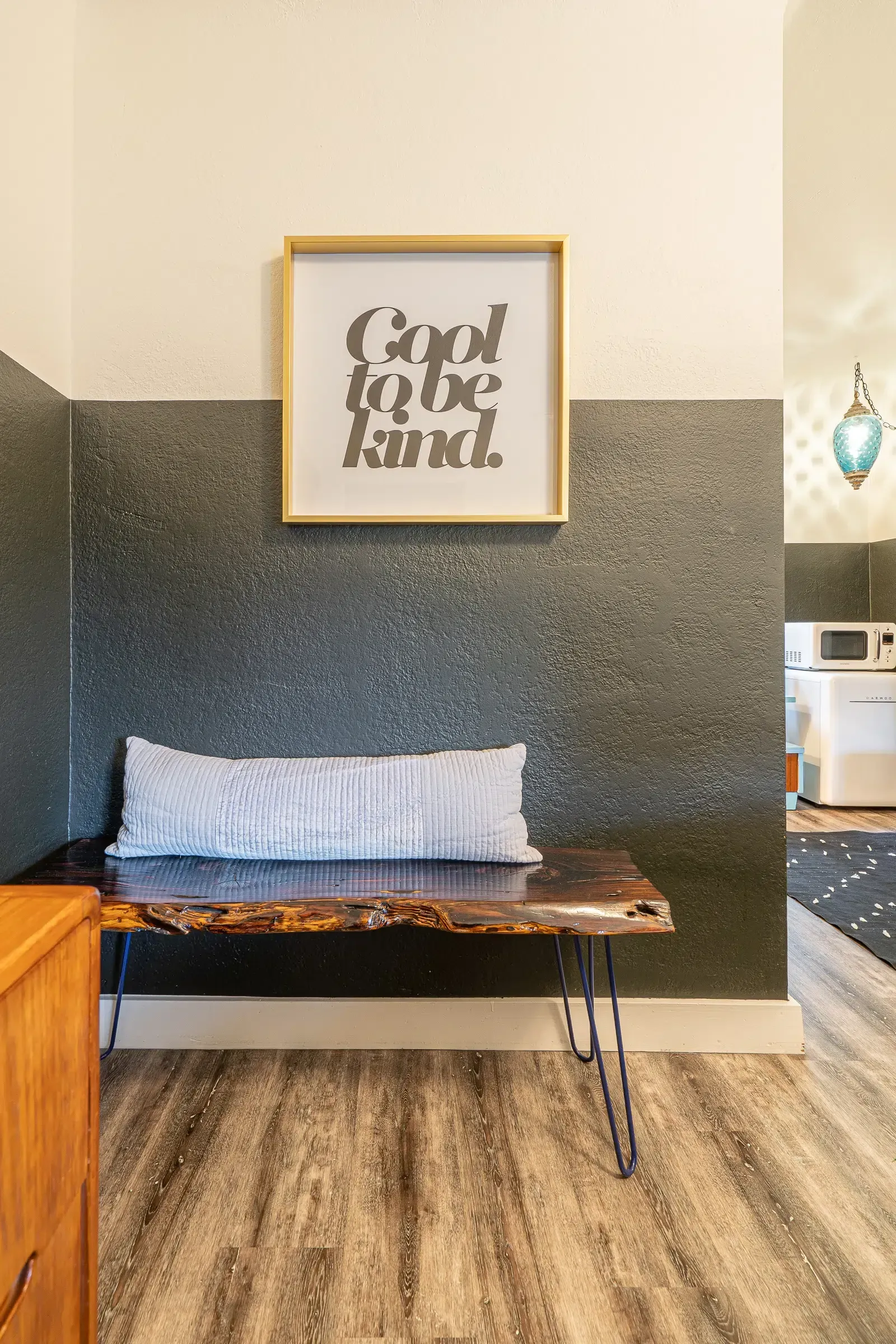 A room with a bench and a picture on the wall that says `` good to be kind ''.