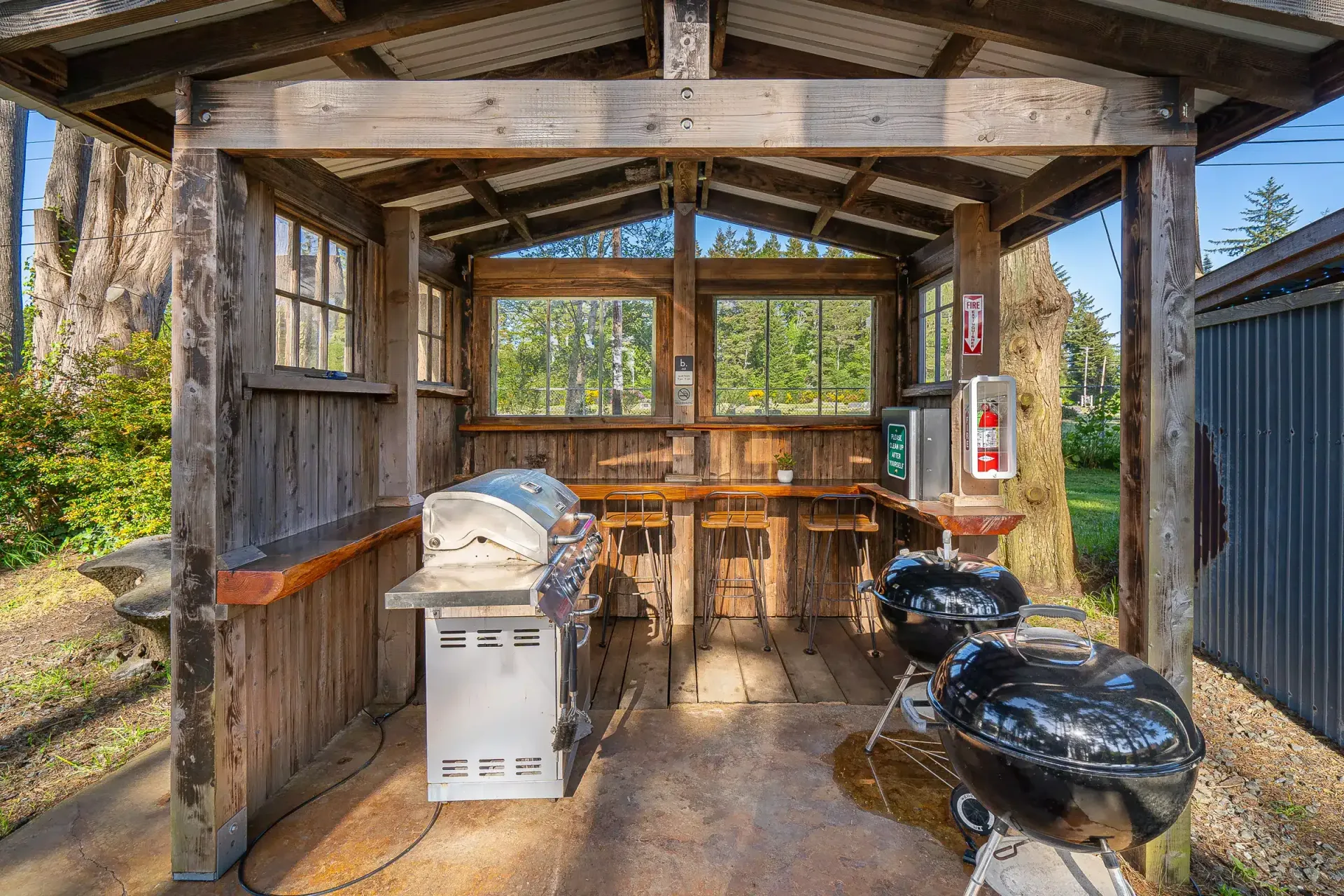 A wooden shelter with a grill and a fire extinguisher.