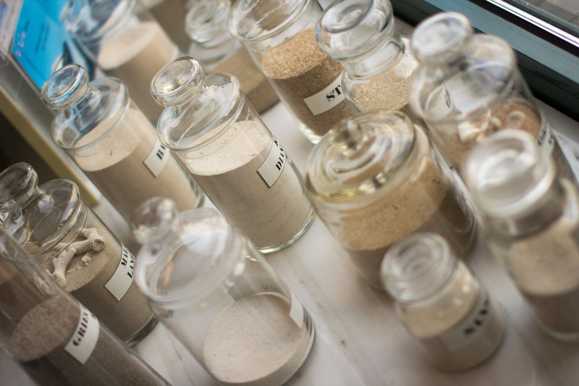 Auf einem Tisch stehen mehrere mit unterschiedlichen Sandarten gefüllte Gläser.