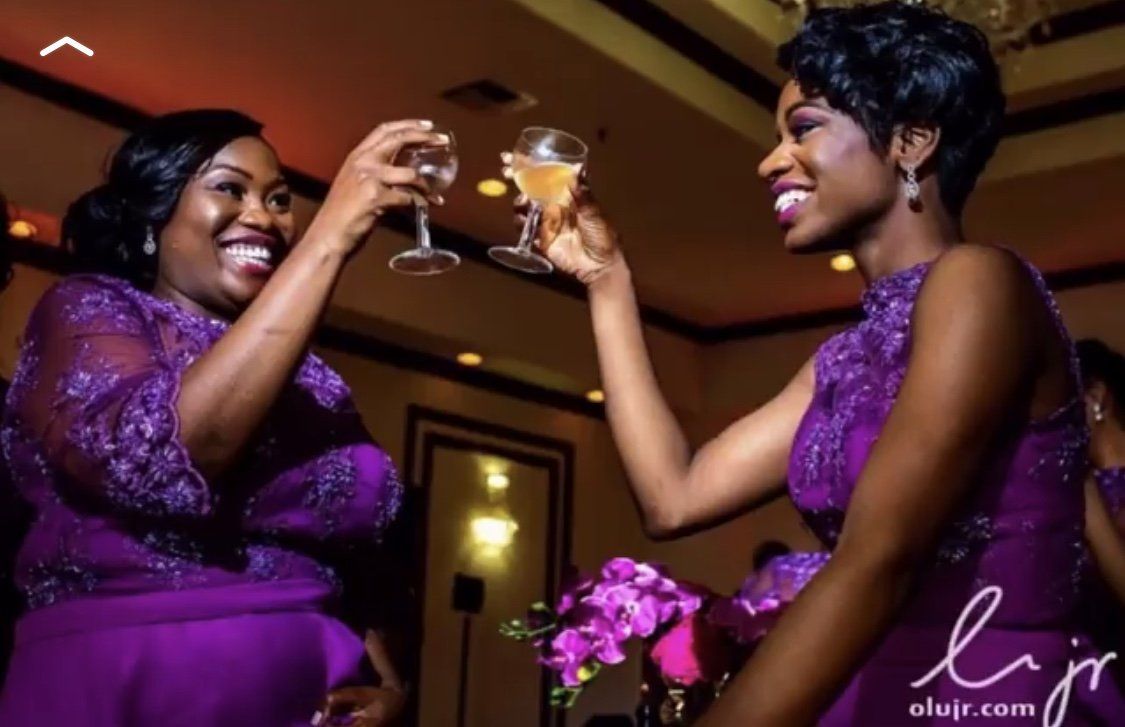 Two women in purple dresses are toasting with champagne glasses