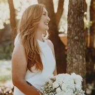 Woman in a white dress holding a bouquet of white flowers outdoors near trees
